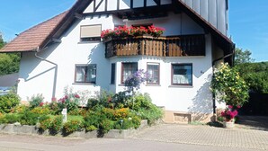 Ein zweistöckiges Haus mit Balkon, Satellitenschüssel und einem Garten mit verschiedenen Blumen.