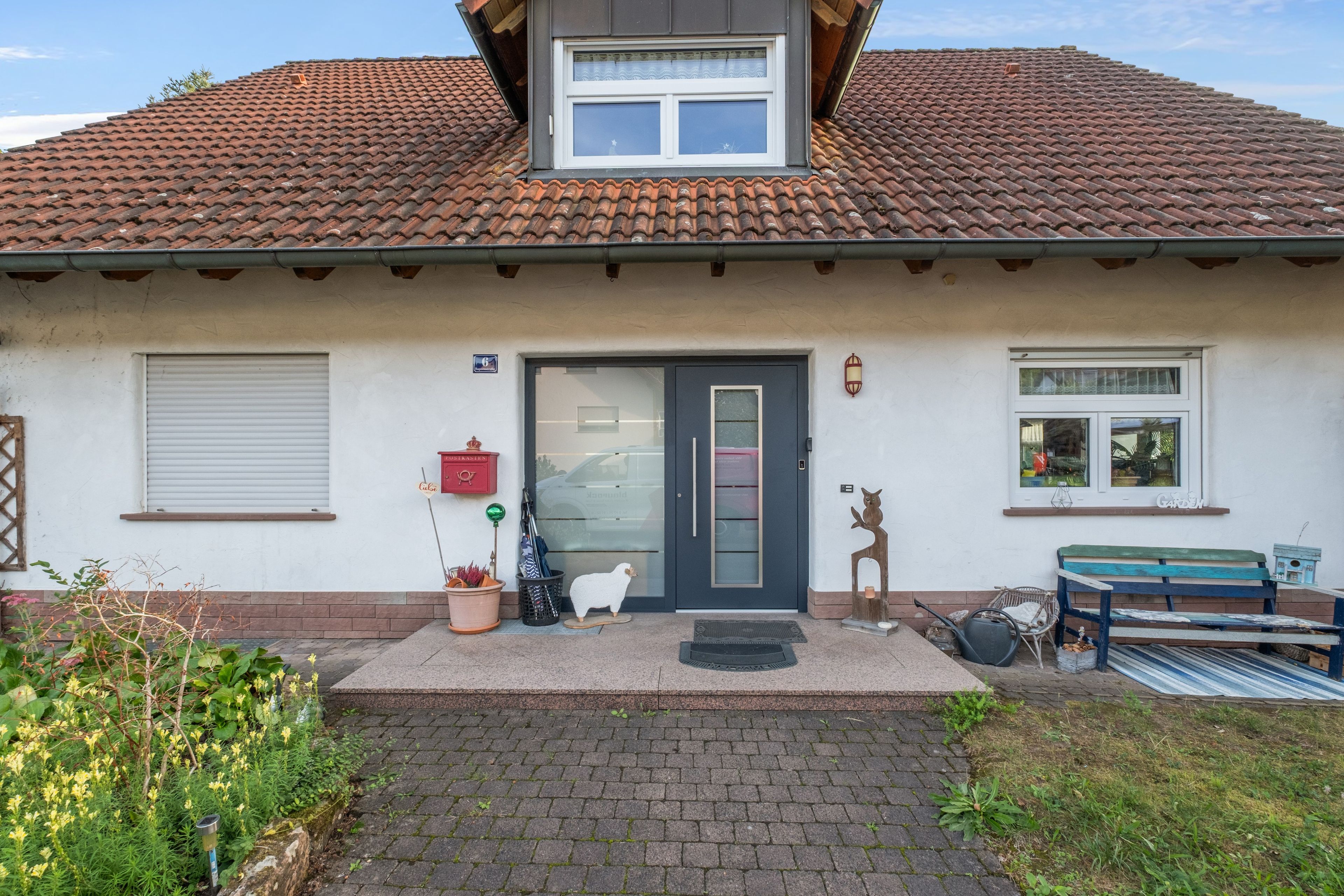 Een huis met pannendak, een voordeur, een brievenbus, een bankje en een kleine tuin.