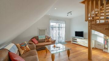 En moderne stue med sofa, sofabord, fjernsyn og trappe.