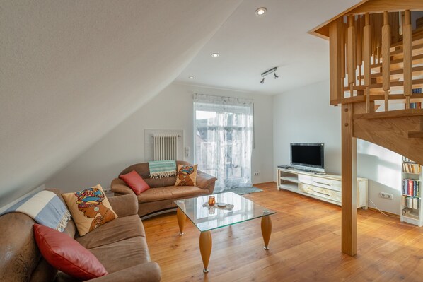 A modern living room with a sofa, coffee table, TV, and a staircase.