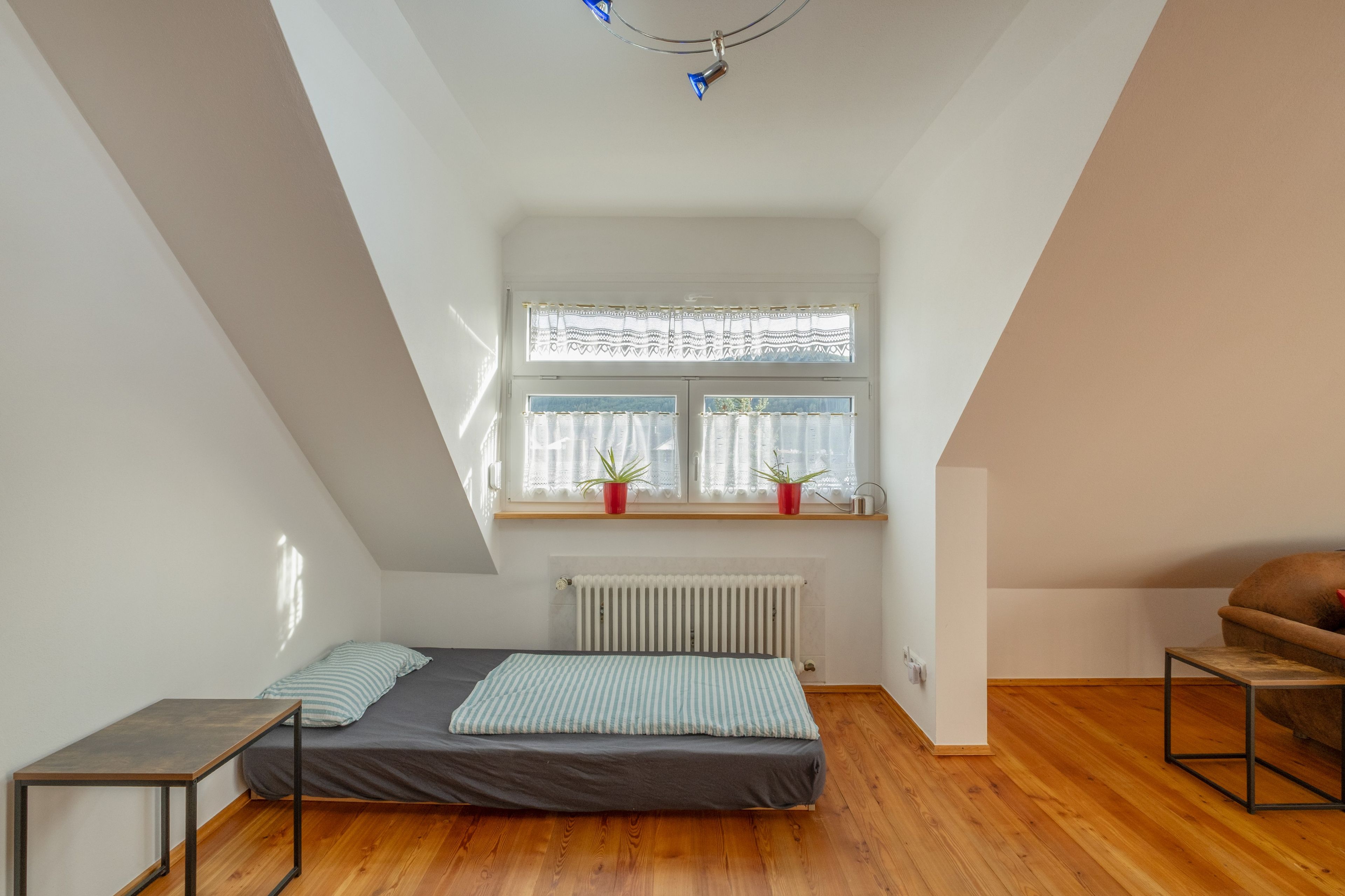 Ein kleiner, gut beleuchteter Raum mit einem Bett, einem Tisch, einem Stuhl und einem Fenster mit Vorhängen.