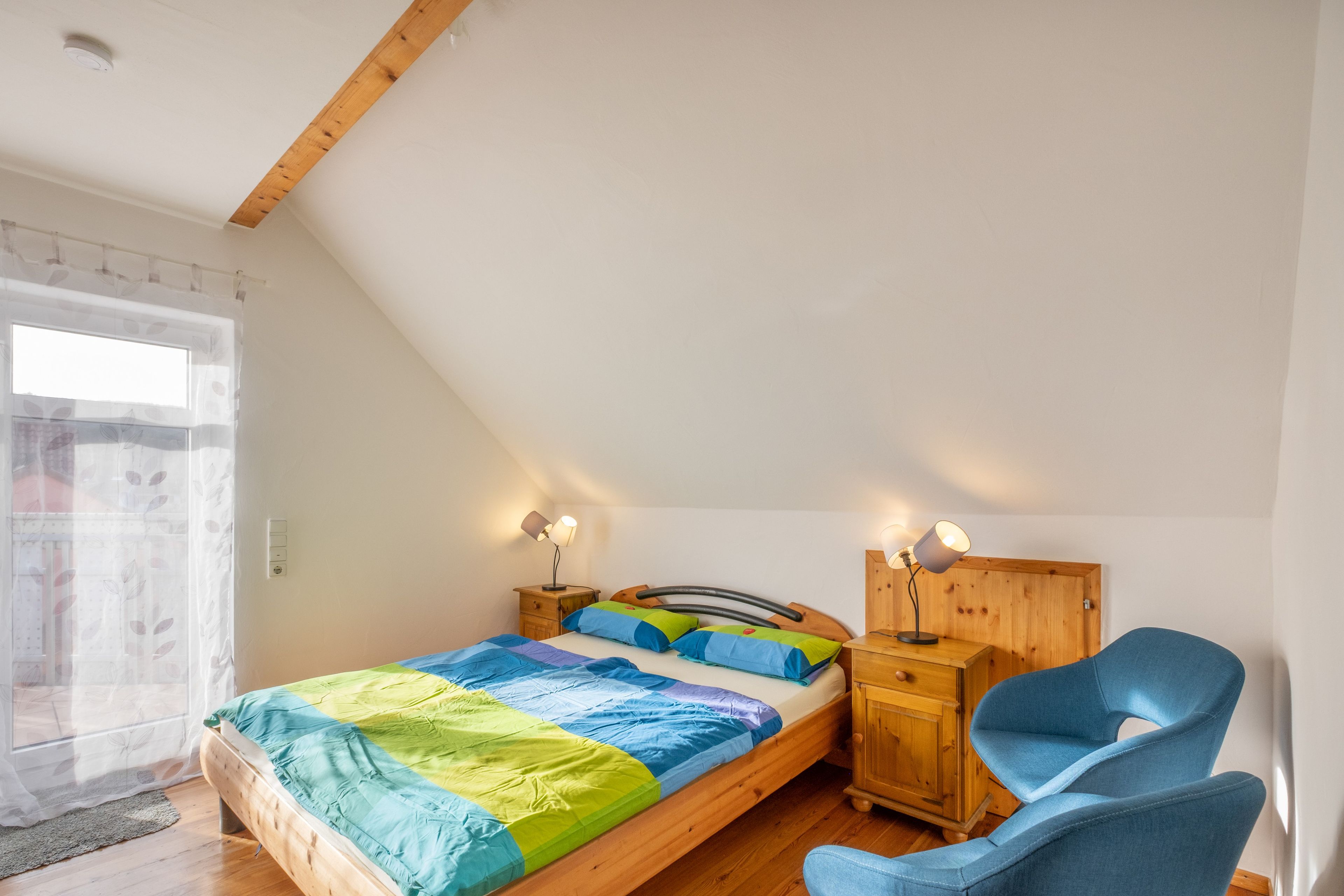 Een slaapkamer met een houten bed, twee nachtkastjes, een stoel en een raam met gordijn.
