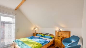 Een slaapkamer met een houten bed, twee nachtkastjes, een stoel en een raam met gordijn.