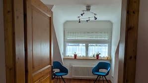 Una habitación con puerta de madera, dos sillas azules, un radiador y una ventana con persianas.