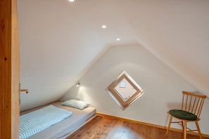 A small, sloped ceiling room with a bed, a chair, and a window.