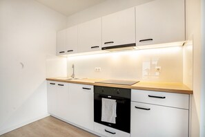 A modern kitchen with white cabinets, a wooden countertop, a black oven, and a stainless steel faucet.