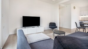 A modern living room with a flat-screen TV, a grey sofa, a small round table, and a dining area with chairs and a kitchen in the background. - Apartment “Loft Am Botanischen Garten” with Balcony and Wi-Fi (Greifswald)
