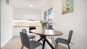 A modern kitchen with white cabinets, a round dining table with four chairs, and a vase with flowers. - Apartment “Loft Am Botanischen Garten” with Balcony and Wi-Fi (Greifswald)