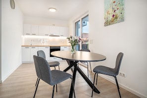 Une cuisine moderne avec des meubles blancs, une table de salle à manger ronde entourée de quatre chaises et un vase rempli de fleurs.