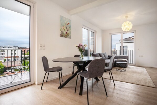 A modern living room with a dining table, chairs, a sofa, and a large window with a view of buildings.