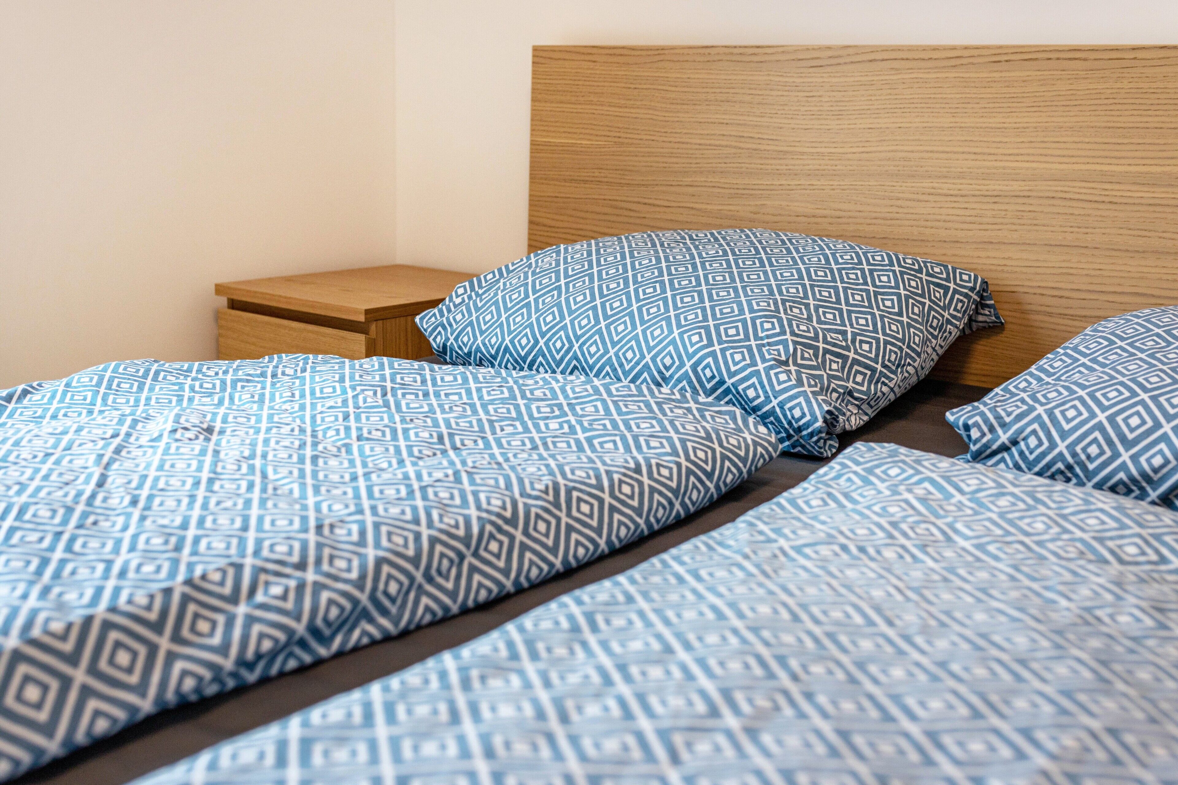 Una cama con colcha y almohadas de estampado geométrico, cabecera de madera y mesita de noche.