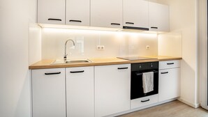 A modern kitchen with white cabinetry, a wooden countertop, a stainless steel sink, a black oven, and a built-in range hood. - Apartment “Loft Am Botanischen Garten” with Balcony and Wi-Fi (Greifswald)