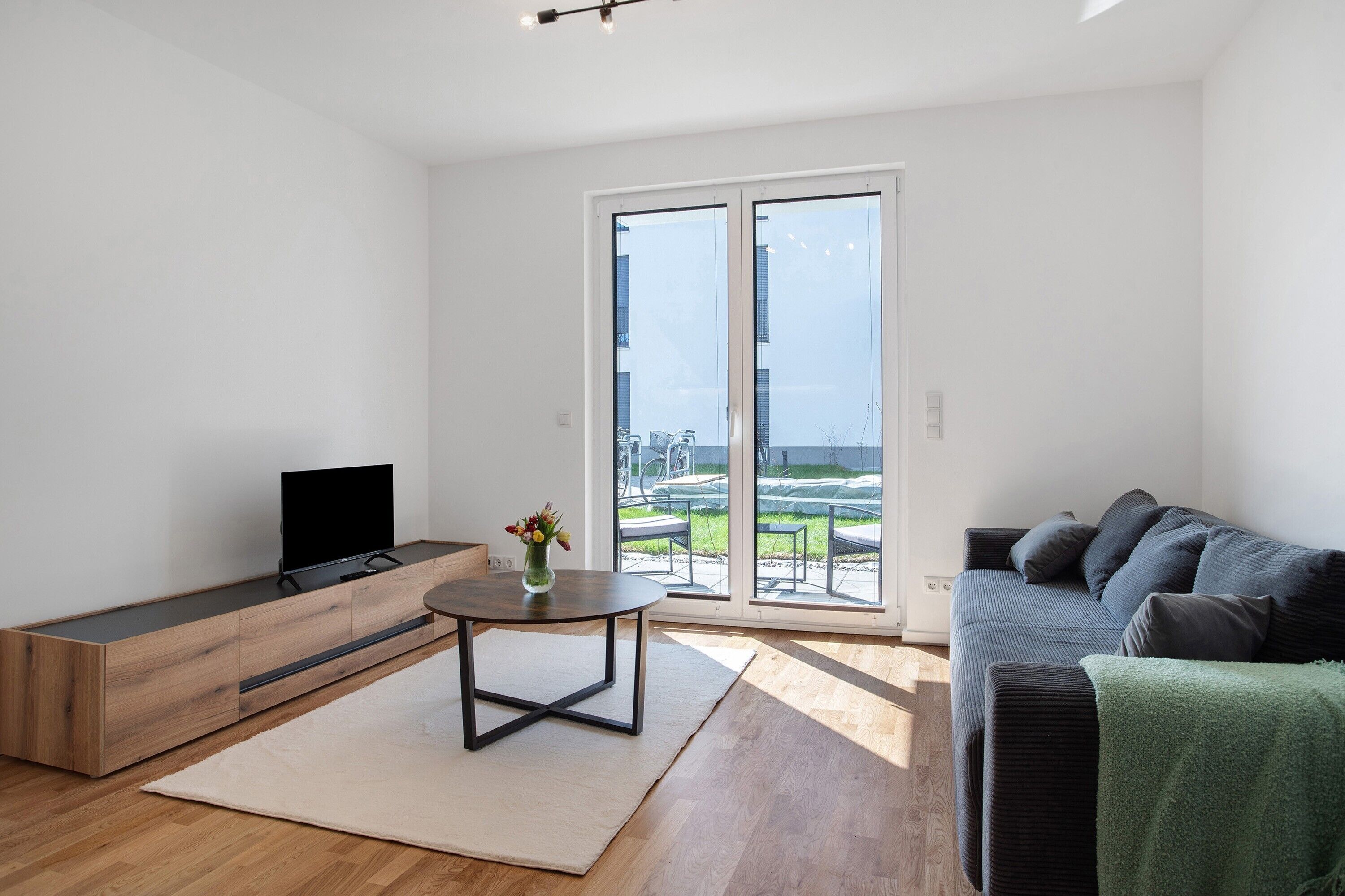 Ein modernes Wohnzimmer mit Flachbildfernseher, rundem Couchtisch, Sofa und einer Schiebetür zu einer Außenpatio.