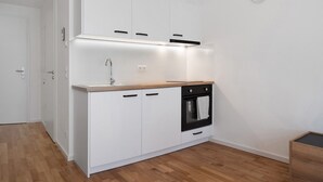 A modern kitchen with white cabinets, a wooden countertop, a built-in oven, and a clock on the wall. - Terrace Loft by the Botanical Garden (Greifswald)