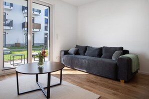 Una sala de estar moderna con un sofá, una mesita redonda y vistas a un balcón con mobiliario exterior.