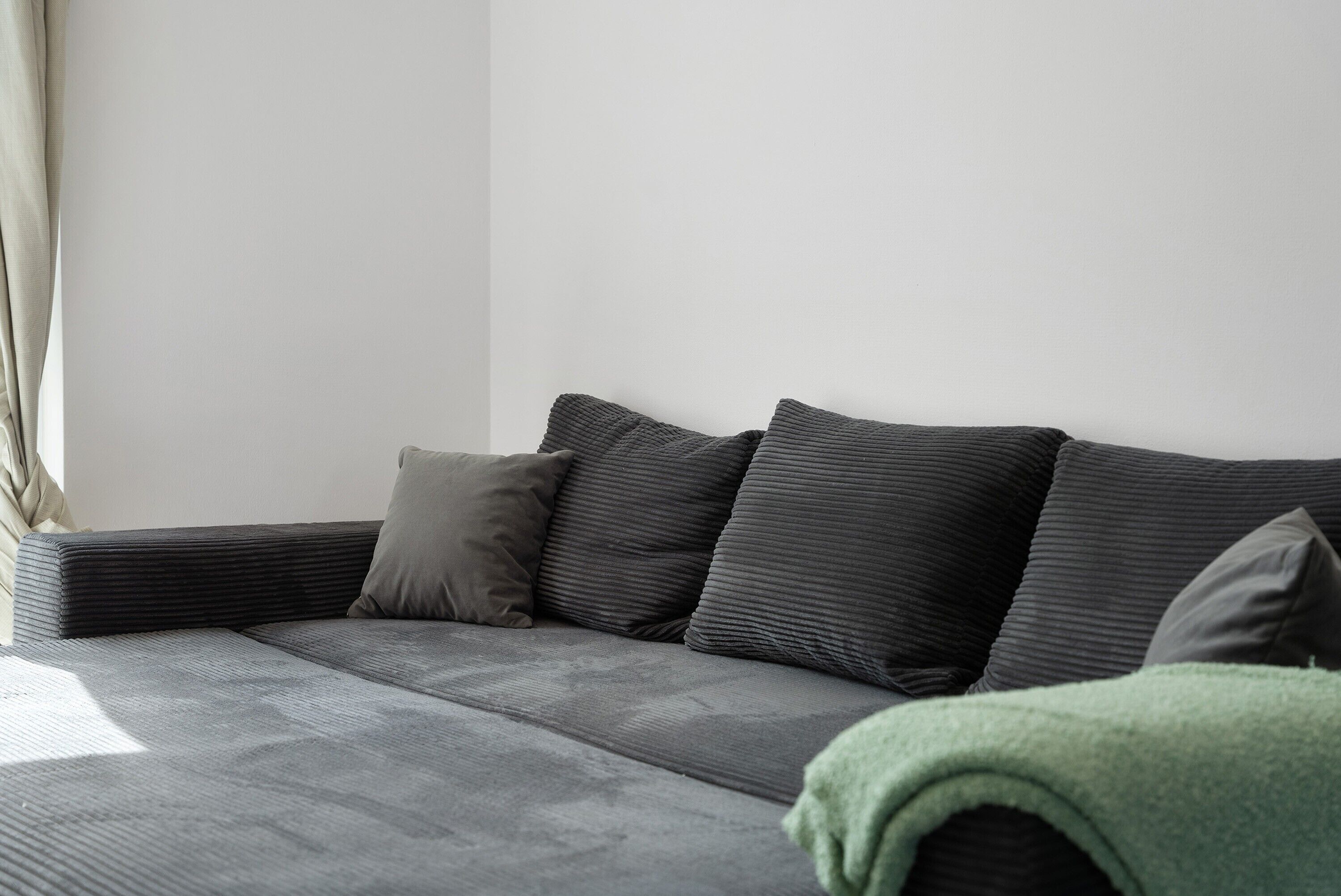 Ein modernes Sofa mit strukturierter Stoffbezug, einer grünen Decke und einem Fenster mit Vorhängen.