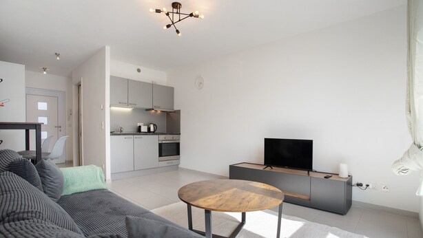 A modern living room with a sofa, a round coffee table, a television, and a kitchen in the background. - Apartment 'Top Location with Cathedral View' with Wi-Fi (Greifswald)