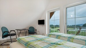 Quarto com duas camas, televisão, escrivaninha e cadeiras, com vista para um lago e colinas.