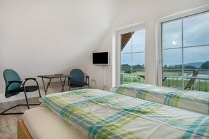 Ein Schlafzimmer mit zwei Betten, einem Fernseher, einem Schreibtisch und Stühlen, mit Blick auf einen See und Hügel.