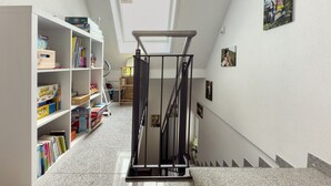 Um corredor estreito com claraboia, estantes de livros, escada e quadros nas paredes.