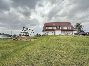 A two-story house with a red roof, a swing set, and a parked car.