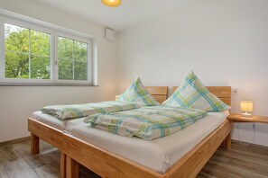 Ein Einzelbett mit Holzrahmen, ein Nachttisch mit Lampe und ein Fenster mit Blick auf Bäume.