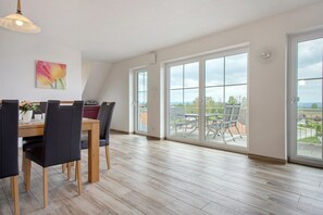 Un espace repas avec une table et des chaises en bois, de grandes fenêtres et une vue sur l’extérieur.