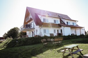 Une maison à deux étages avec un balcon, une terrasse en bois et une table de pique-nique dans le jardin.
