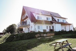 Ein zweistöckiges Haus mit Balkon, einer Holzterrasse und einem Picknicktisch im Garten.