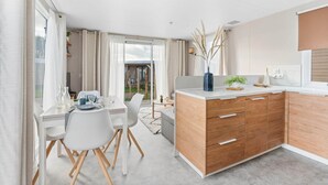 Eine moderne Küche mit Holzschränken, einer weißen Arbeitsplatte und einem Essbereich mit weißem Tisch und Stühlen.