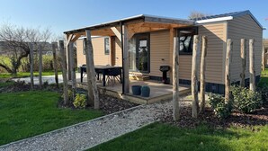 A small, single-story wooden cabin with a covered patio area, a dining table, and a chair.
