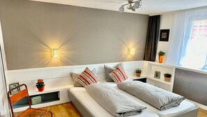 A modern bedroom with a bed, bedside tables, a chair, and wall-mounted lighting.