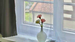 A window with a view of a traditional building, a vase with flowers, and a curtain.
