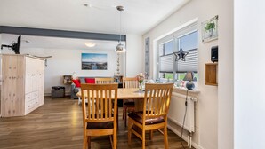 Een eethoek met een houten tafel en stoelen, een radiator, een raam met zonwering en uitzicht op de omgeving.