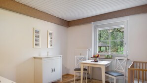 Een kamer met houten vloer, witte wanden, een raam met uitzicht op groen, een wit bureau met stoel en een witte kast.