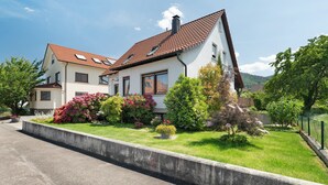 Ein zweistöckiges Haus mit einem geneigten Dach, einer Betonauffahrt und einem gepflegten Garten mit verschiedenen Pflanzen und Blumen.