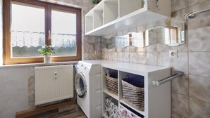 A laundry area with a washing machine, shelves with baskets, a radiator, and a window with a view. - Apartment 'Moos' with Private Terrace and Wi-Fi (Argenbühl)