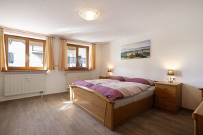 Un dormitorio con cama de madera, dos mesitas de noche, una ventana, un radiador y un cuadro colgado en la pared.
