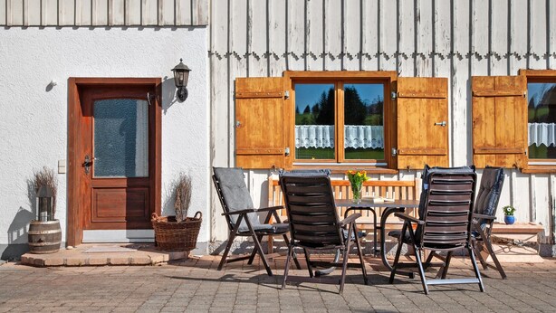 A building with a wooden door, a window with a curtain, and outdoor seating with chairs and a table. - Apartment 'Moos' with Private Terrace and Wi-Fi (Argenbühl)