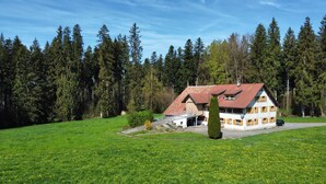 A house with a red roof, surrounded by a green field and dense forest. - Apartment 'Moos' with Private Terrace and Wi-Fi (Argenbühl)