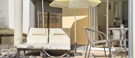 A balcony with two lounge chairs, a yellow umbrella, and a dining table with chairs.