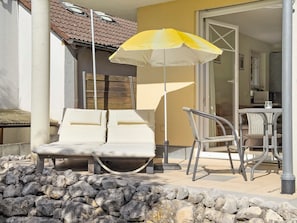 A balcony with two lounge chairs, a yellow umbrella, and a dining table with chairs. - Holiday Apartment 'Jacqueline' with Private Terrace, Shared Garden and Wi-Fi (Uhldingen-Mühlhofen)