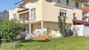 Une maison à deux étages avec un balcon, un mur en pierre et un banc en bois.