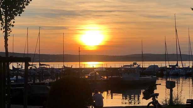 Un port de plaisance avec des bateaux amarrés, un coucher de soleil en arrière-plan et une personne à vélo.
