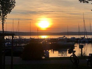 En småbåtshamn med förtöjda båtar, en solnedgång i bakgrunden och en person på en cykel.