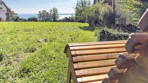 Un champ verdoyant avec un banc en bois, un bâtiment doté d’un toit en tuiles et une vue lointaine sur la mer.