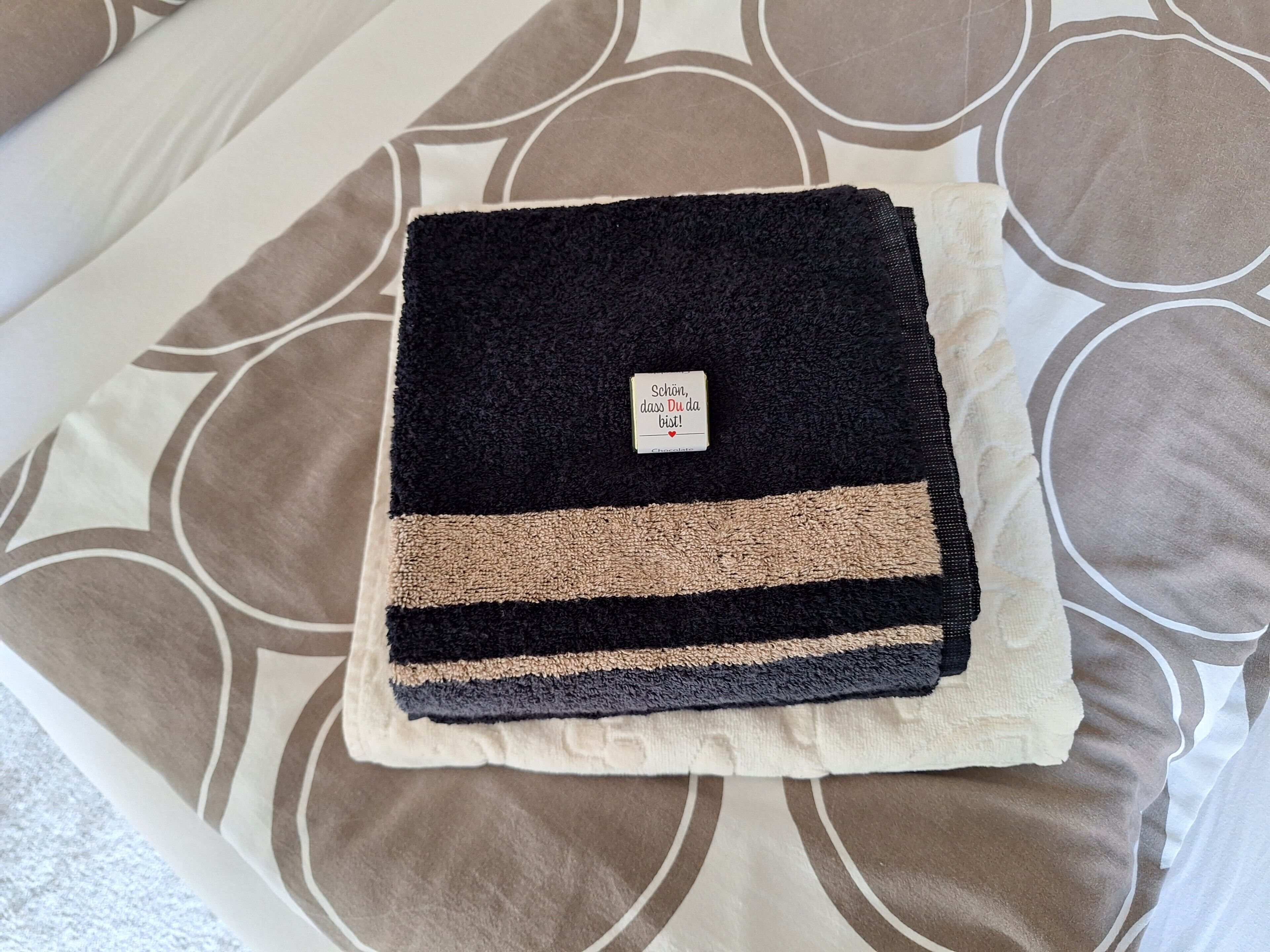 Ein ordentlich gefaltetes schwarzes und beiges Handtuch auf einer gestreiften Tagesdecke.
