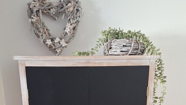 Une pièce avec une armoire en bois foncé, une décoration en forme de cœur et une plante posée sur le dessus.