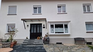 Un bâtiment à deux étages avec une porte d’entrée noire, des fenêtres blanches et une entrée pavée de pierres.