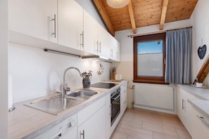Una cucina con mobili bianchi, un lavello in acciaio inossidabile, forno integrato e una finestra con tende.